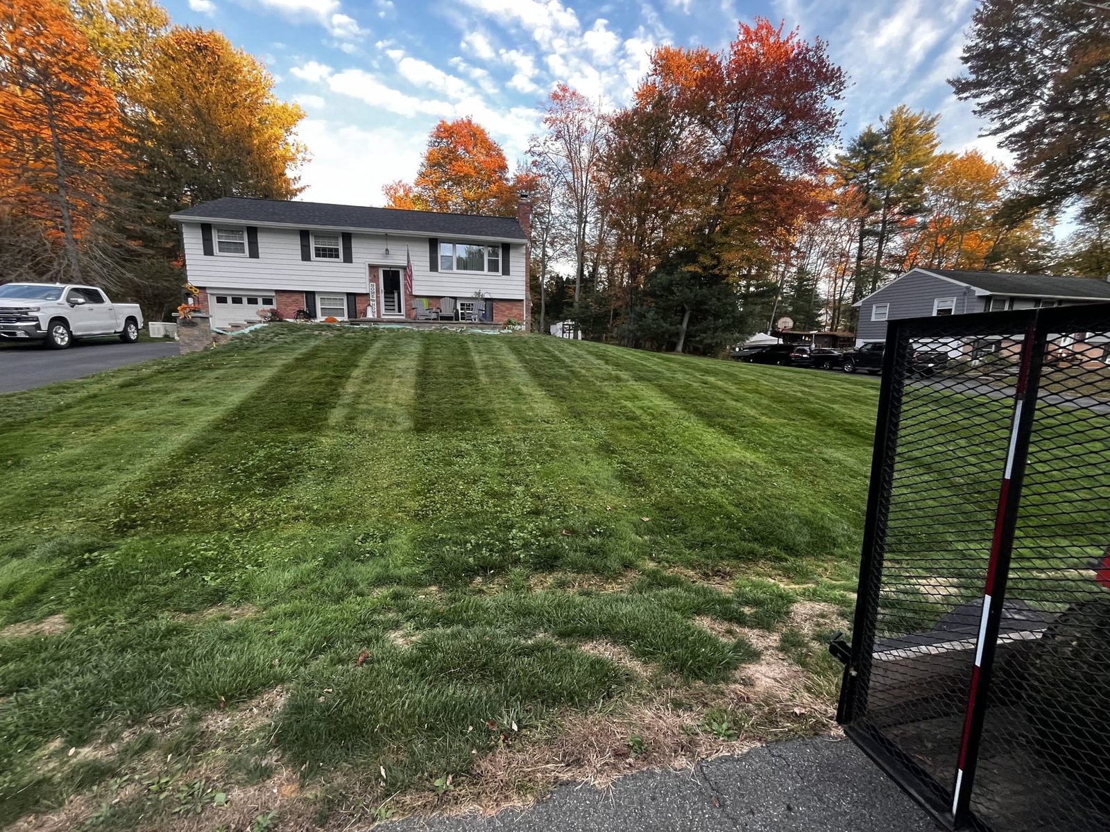 Striped front lawn with fall foliage, trailer visible at right edge of frame