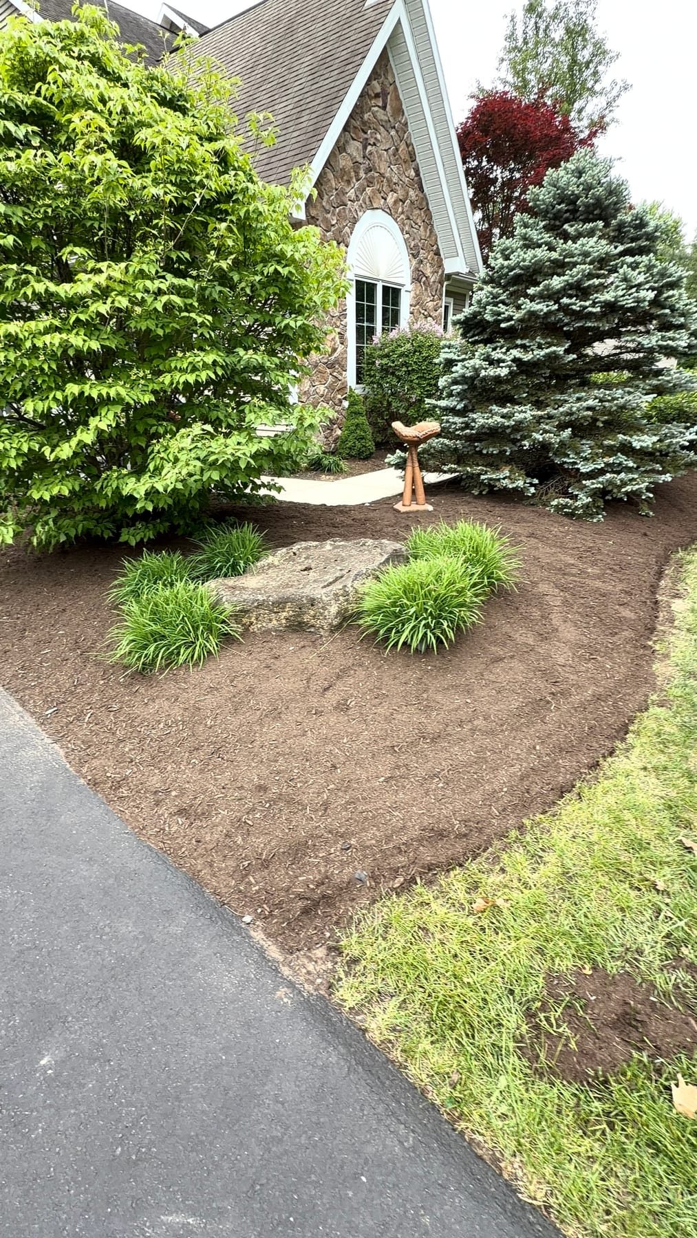 Stone-front home with shaped shrubs, decorative stone, conifer and freshly installed mulch beds