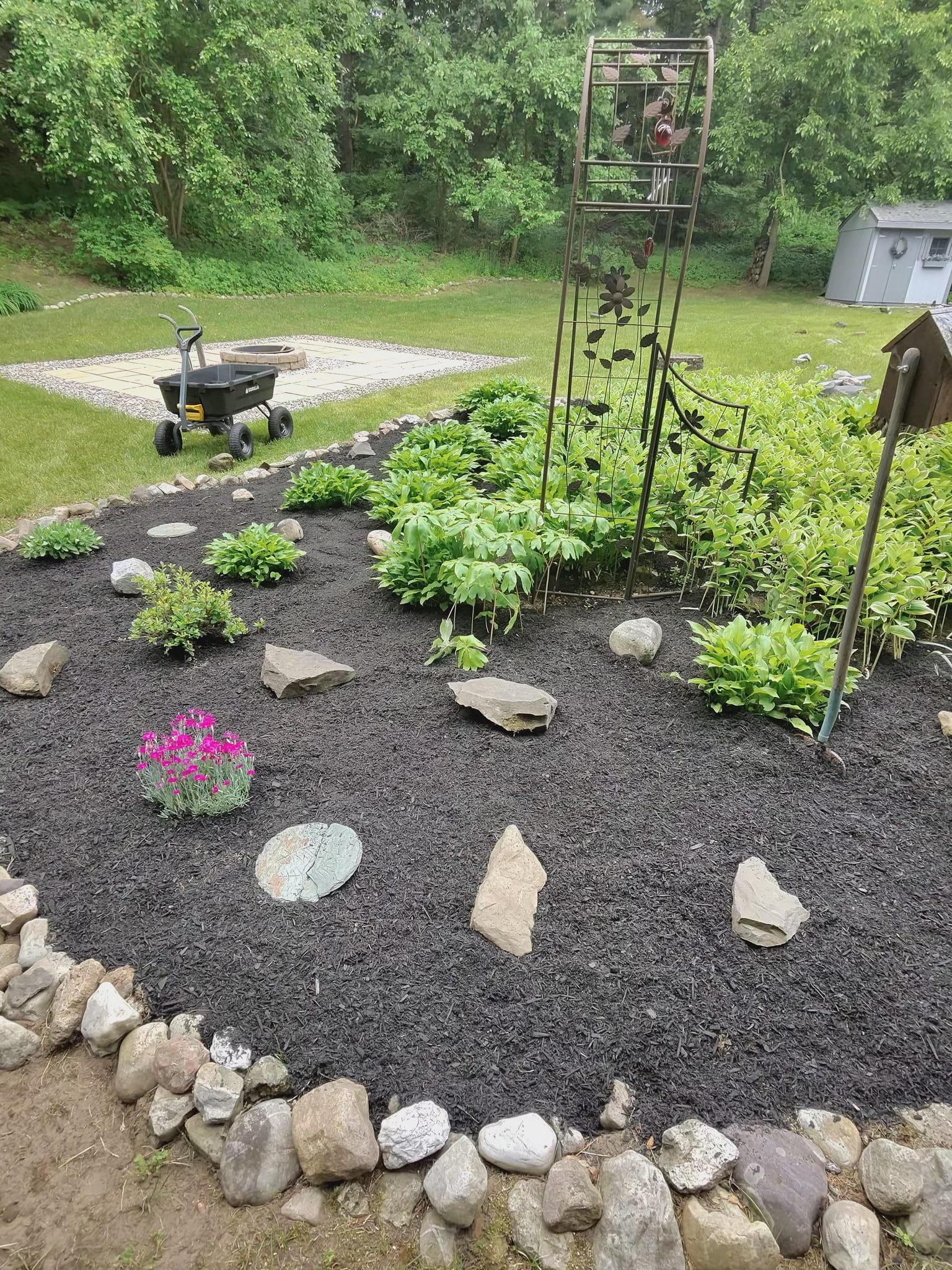 A planted garden bed edged with a curved stone border beside a wooden trellis.