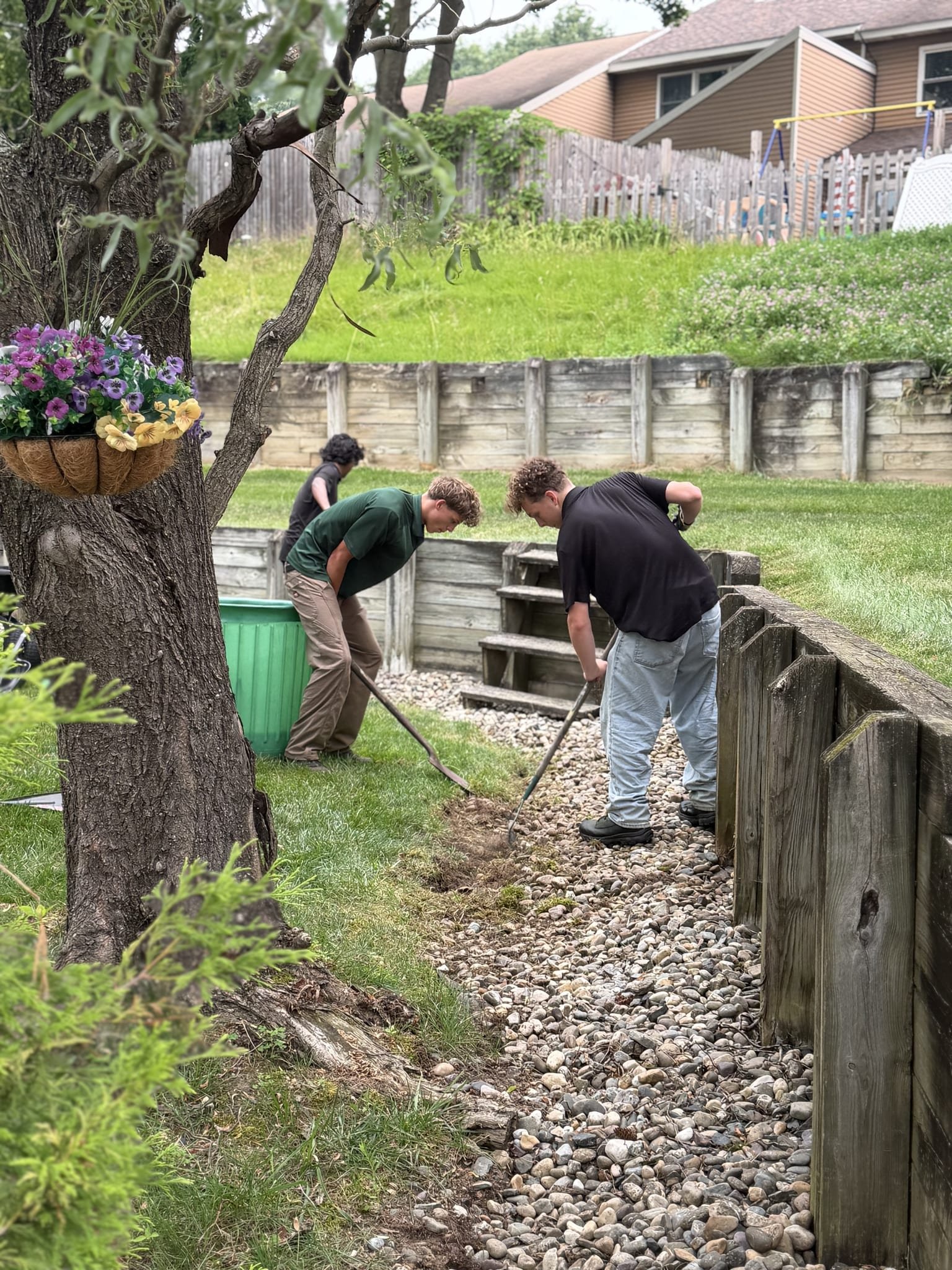 Three crew members re-edging a stone drainage bed along a retaining wall