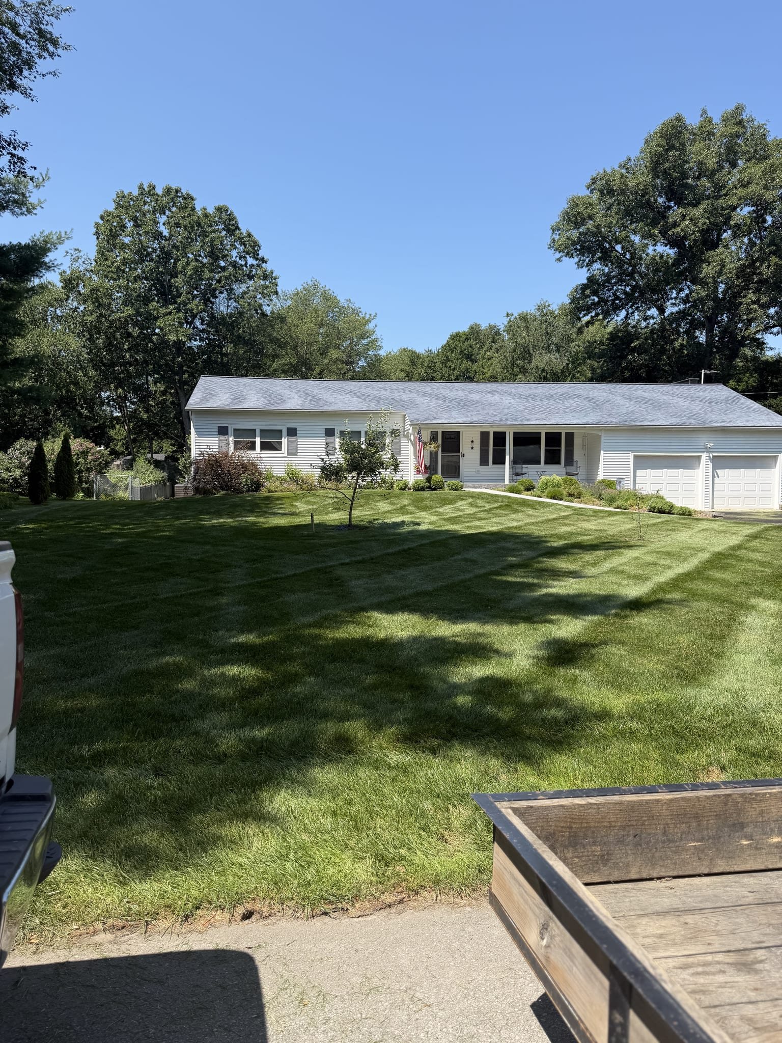 Wide striped front lawn of a white ranch home with a flag on the porch
