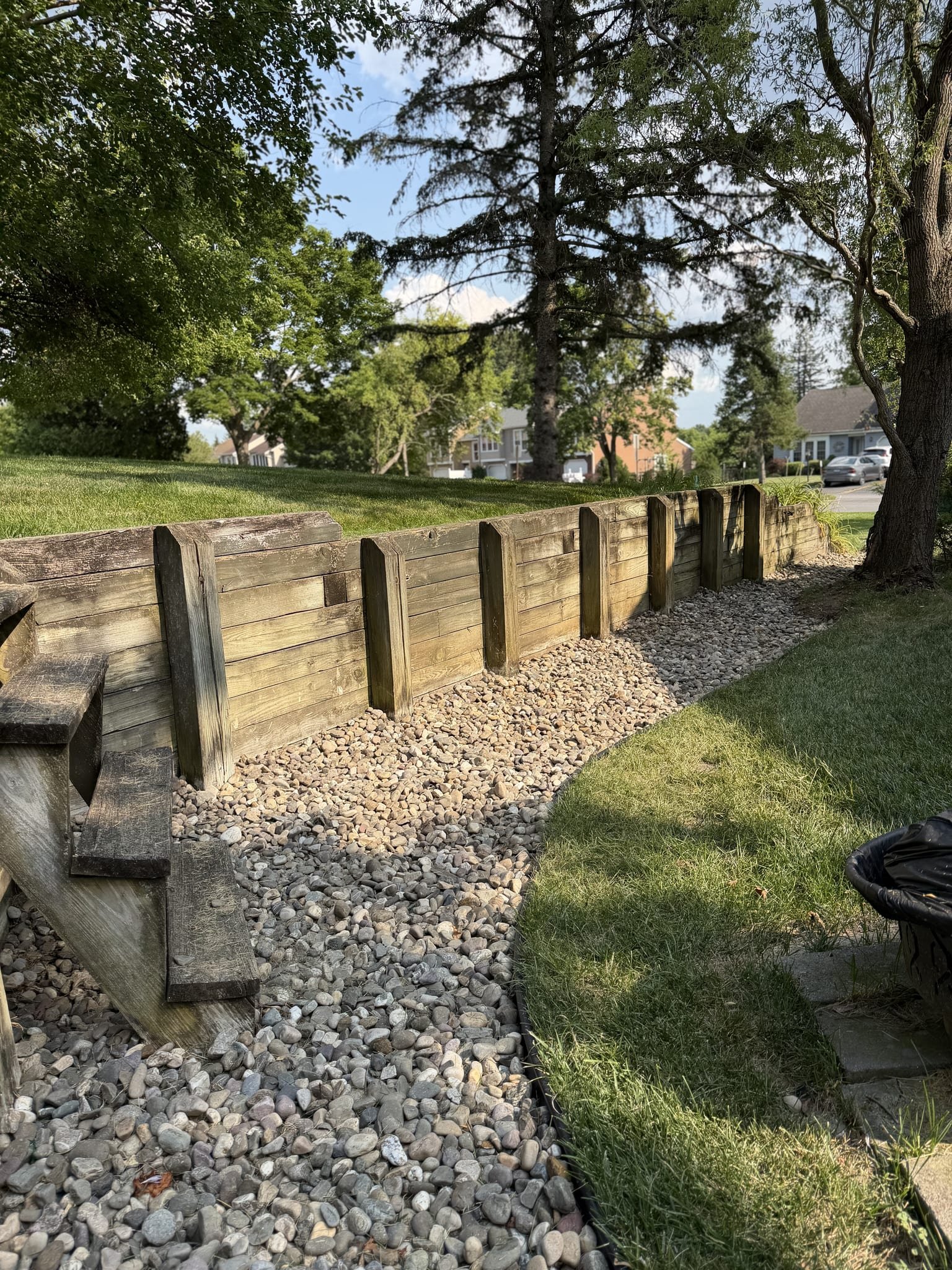 Clean river-rock drainage bed running along a timber retaining wall