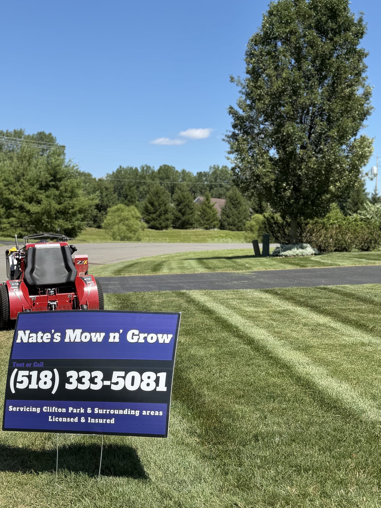 Nate's Mow n' Grow yard sign staked in a freshly striped lawn with the mower behind it