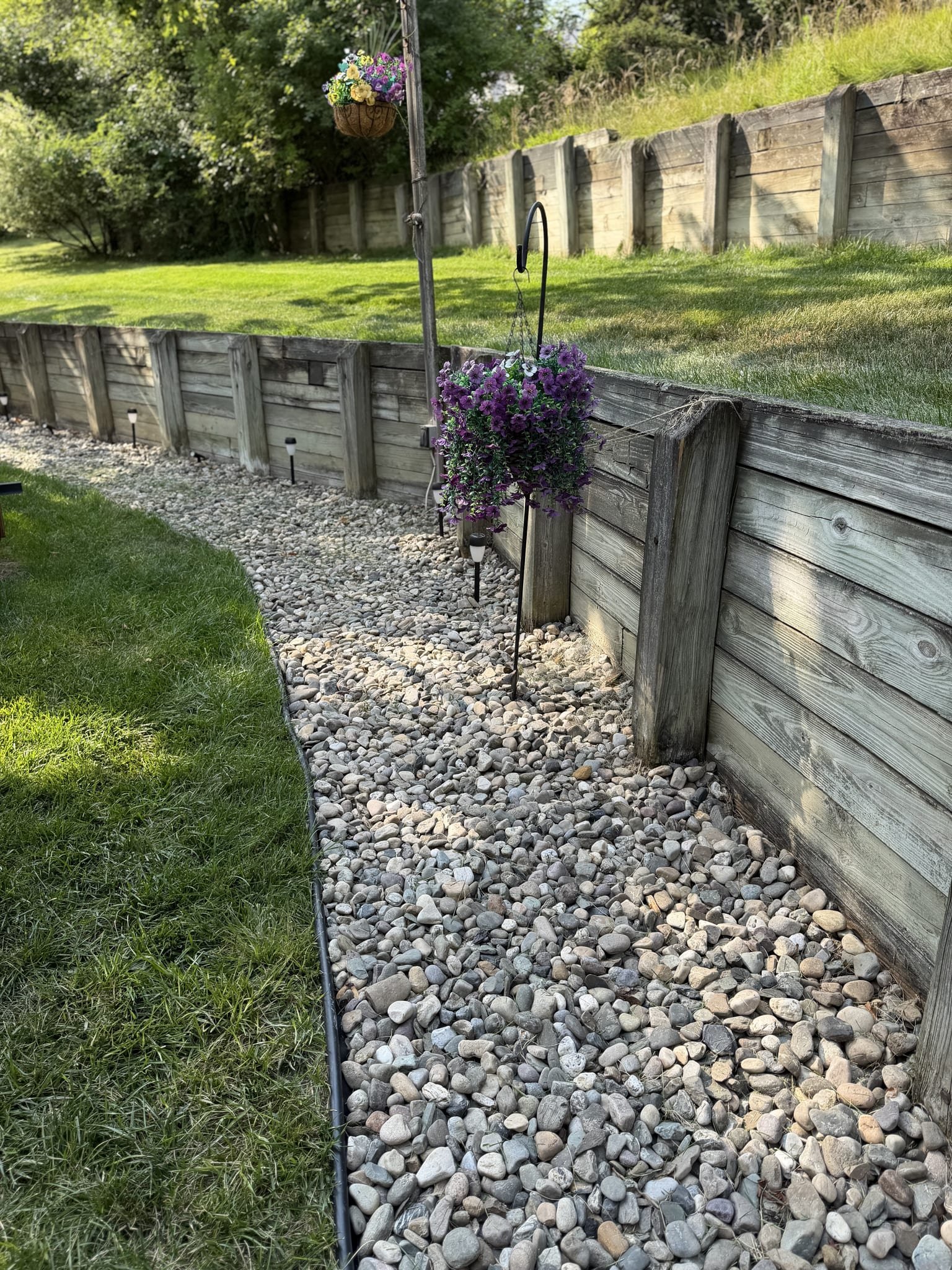 River-rock border along a timber retaining wall with hanging flower baskets