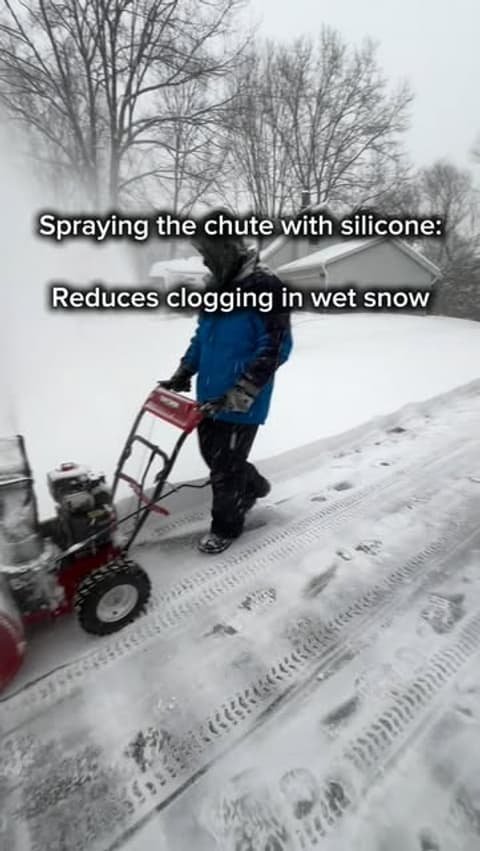 Crew member clearing a driveway with a snow blower during a storm