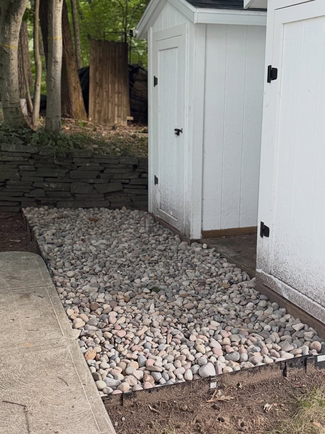 New river rock bed with clean metal edging running alongside a white shed